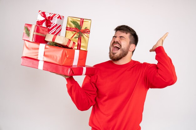 Vista frontal del joven en camisa roja con regalos de Navidad en la pared blanca