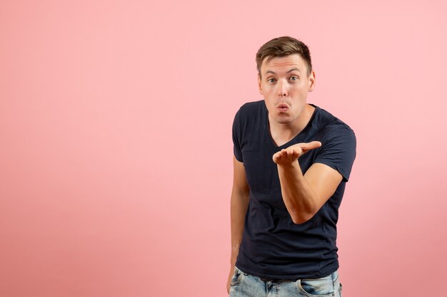 Vista frontal joven en camiseta azul enviando besos al aire sobre fondo rosa emoción modelo de color humano masculino