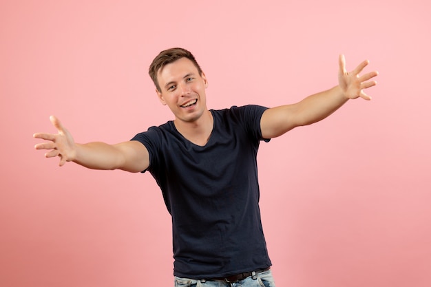 Vista frontal joven en camiseta azul en pose de bienvenida sobre fondo rosa emoción modelo de color humano masculino