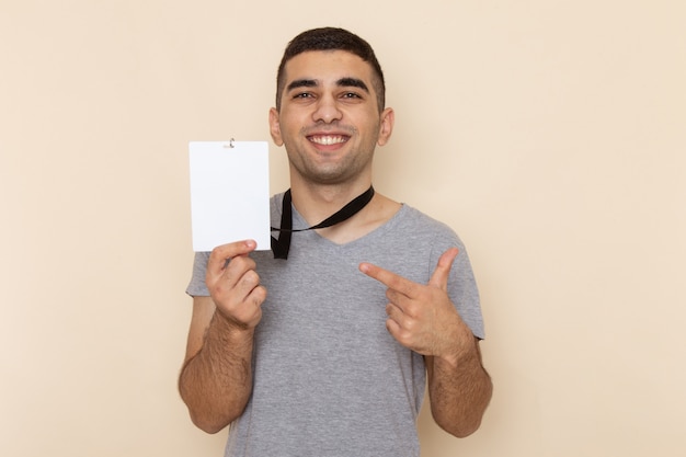 Vista frontal joven en camiseta gris con tarjeta de identidad con sonrisa en beige