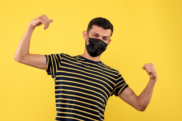 Vista frontal joven en camiseta a rayas blanco y negro mostrando fuerza sobre fondo amarillo