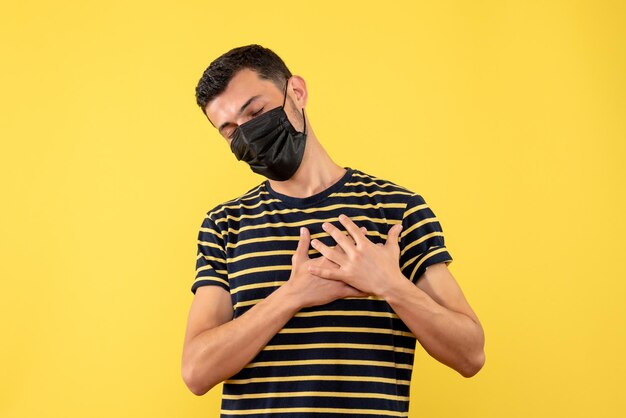 Vista frontal joven en camiseta a rayas blanco y negro poniendo las manos sobre su pecho fondo amarillo