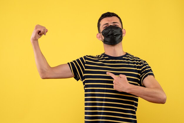 Foto gratuita vista frontal joven con camiseta a rayas en blanco y negro que muestra el músculo del brazo fondo amarillo