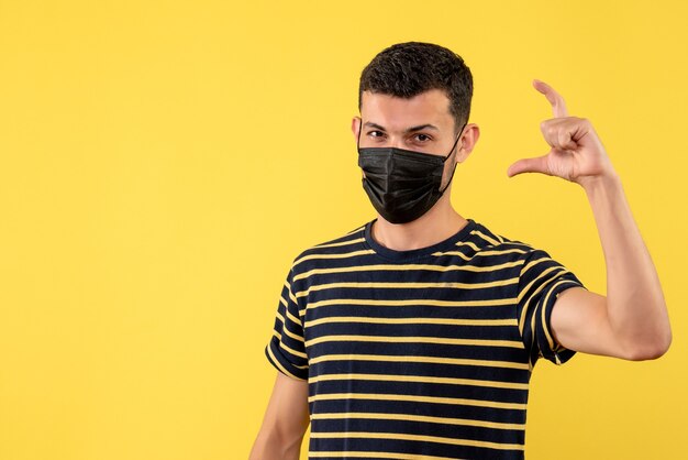 Vista frontal joven en camiseta a rayas blanco y negro que muestra el tamaño con los dedos sobre fondo amarillo