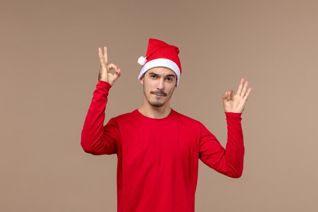Vista frontal joven con capa roja de Navidad sobre fondo marrón emoción vacaciones macho