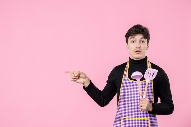 Vista frontal joven en capa sosteniendo cucharas rosadas sobre fondo rosa profesión comida trabajo horizontal cocinar comida masa color uniforme