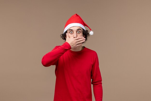 Vista frontal joven con cara de sorpresa sobre fondo marrón Navidad emoción vacaciones