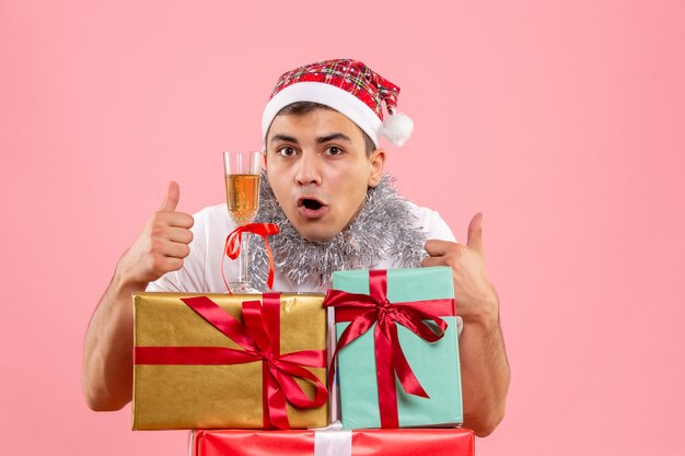 Vista frontal del joven celebrando la Navidad alrededor de regalos en pared rosa