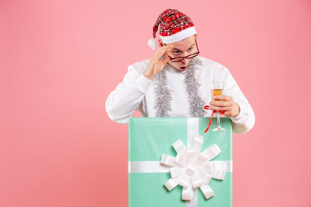 Vista frontal del joven celebrando la Navidad con bebida y guirnaldas en la pared rosa.
