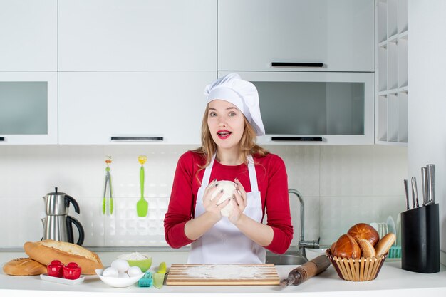 Vista frontal joven chef con gorro de cocinero y delantal sosteniendo la masa en la cocina