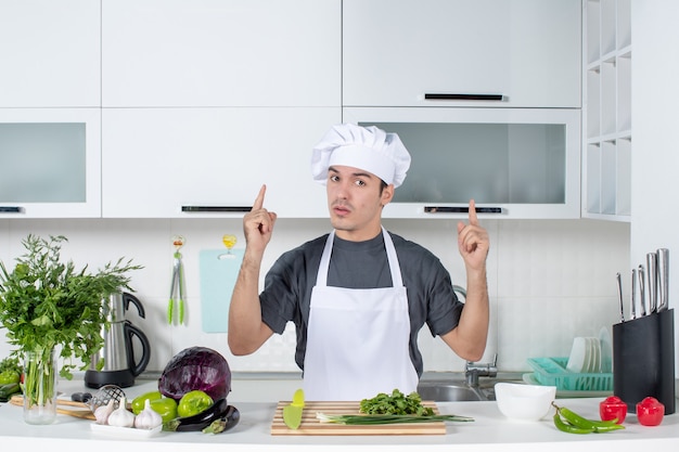 Vista frontal joven chef en uniforme apuntando al techo