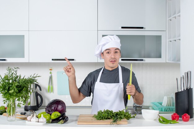 Vista frontal joven chef en uniforme apuntando a la izquierda sosteniendo el cuchillo