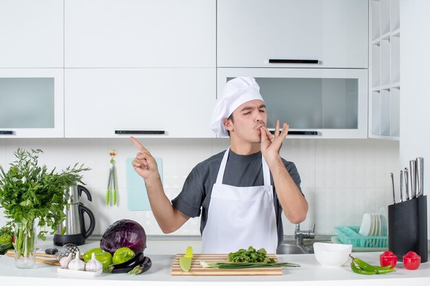 Vista frontal joven chef en uniforme haciendo chef beso en la cocina