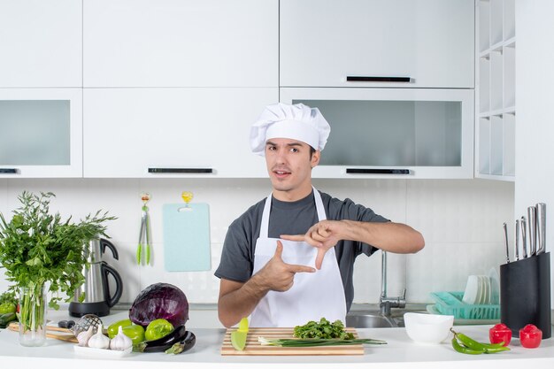 Vista frontal joven chef en uniforme haciendo letrero de cámara