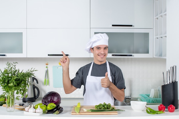 Vista frontal joven chef en uniforme haciendo Thumbs up sign