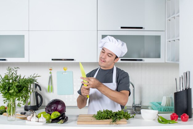 Vista frontal joven chef en uniforme limpiando su cuchillo