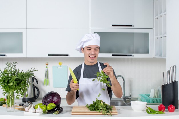 Vista frontal joven chef en uniforme sonriendo mirando verdes
