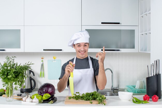 Vista frontal joven chef en uniforme sosteniendo un cuchillo apuntando al techo