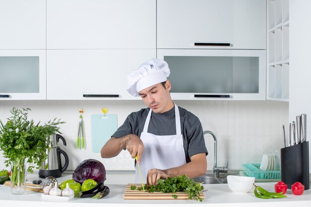 Vista frontal joven chef en verduras de corte uniforme en la mesa