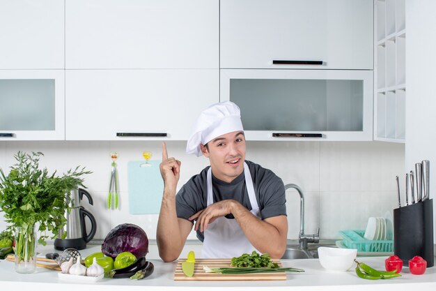 Vista frontal joven chef en verduras de corte uniforme en tabla de cortar