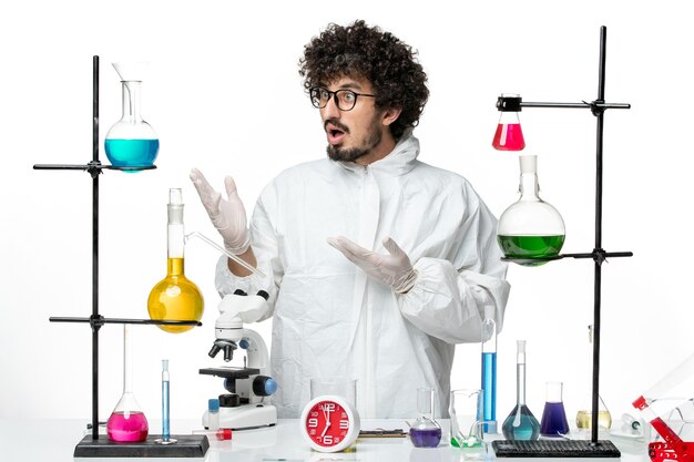 Vista frontal joven científico masculino en traje especial de pie alrededor de la mesa con soluciones en un laboratorio de escritorio blanco