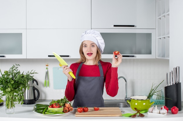 Vista frontal joven cocinera en delantal con cuchillo y tomate