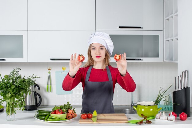 Vista frontal joven cocinera en delantal sosteniendo tomates cortados