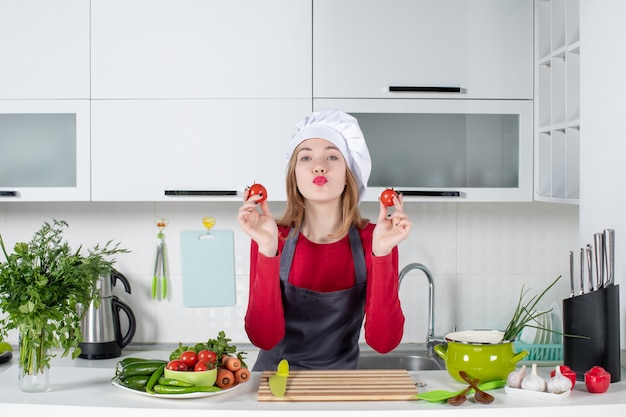 Vista frontal joven cocinera en delantal sosteniendo tomates enviando beso