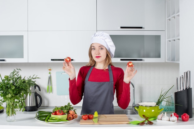 Vista frontal joven cocinera en delantal sosteniendo tomates