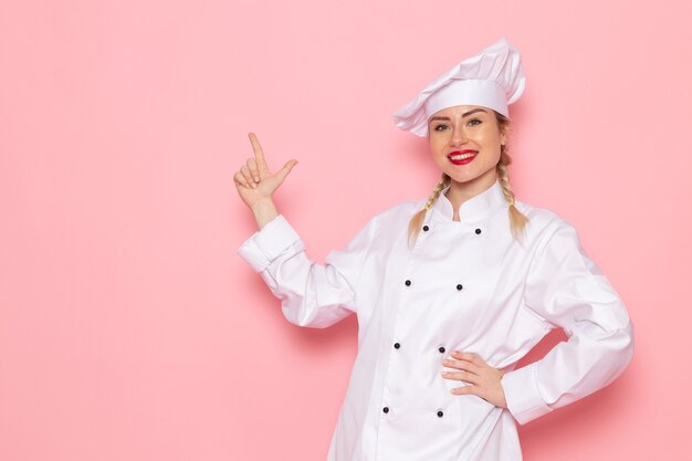 Vista frontal joven cocinera en traje blanco posando sonriendo en el espacio rosa cocinar cocina trabajo trabajo