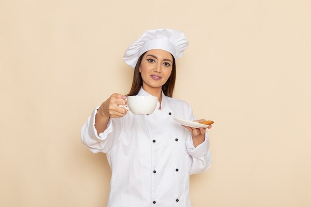 Vista frontal de la joven cocinera en traje de cocinero blanco con café en la pared blanca clara