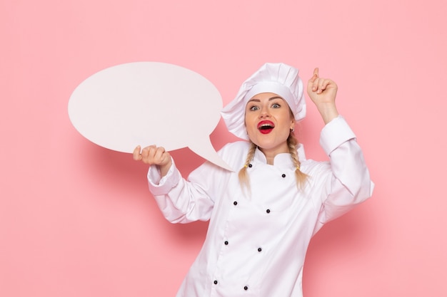 Vista frontal joven cocinera en traje de cocinero blanco con cartel blanco en el espacio rosa cocinero