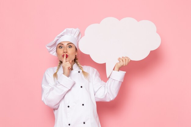 Vista frontal joven cocinera en traje de cocinero blanco con cartel blanco en el espacio rosa cocinero