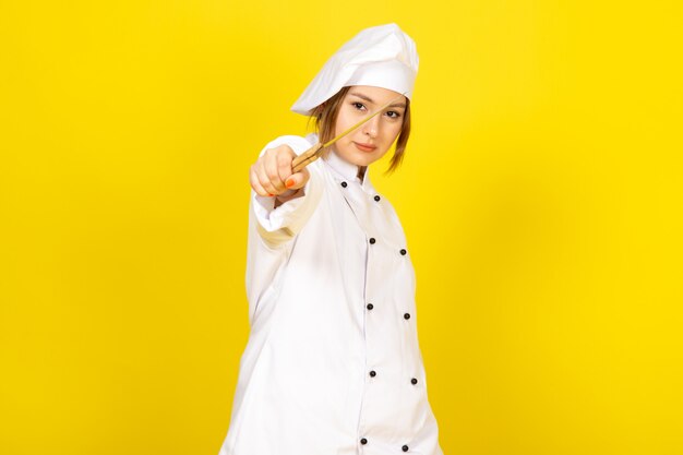 Una vista frontal joven cocinera en traje de cocinero blanco y gorra blanca con cuchillo amenazando en el amarillo