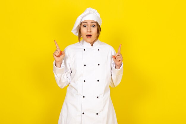 Una vista frontal joven cocinera en traje de cocinero blanco y gorra blanca emocionado expresión en el amarillo