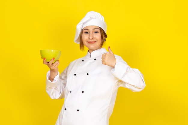 Foto gratuita una vista frontal joven cocinera en traje de cocinero blanco y gorra blanca con placa amarilla encantada sonriendo en el amarillo