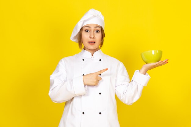 Una vista frontal joven cocinera en traje de cocinero blanco y gorra blanca con placa amarilla sobre el amarillo