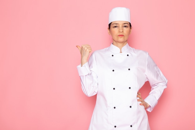 Una vista frontal joven cocinera en traje de cocinero blanco gorra blanca posando disgustado mirada seria con expresión de la mano