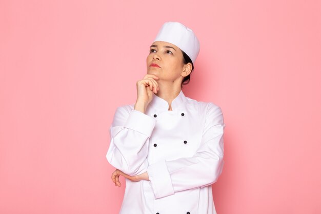 Una vista frontal joven cocinera en traje de cocinero blanco gorra blanca posando expresión de pensamiento profundo