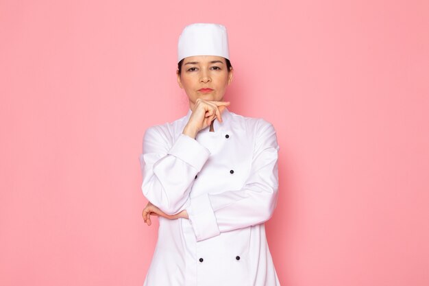 Una vista frontal joven cocinera en traje de cocinero blanco gorra blanca posando expresión de pensamiento profundo