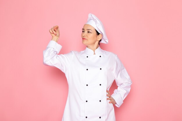 Una vista frontal joven cocinera en traje de cocinero blanco gorra blanca posando sonriendo señalando con sus manos
