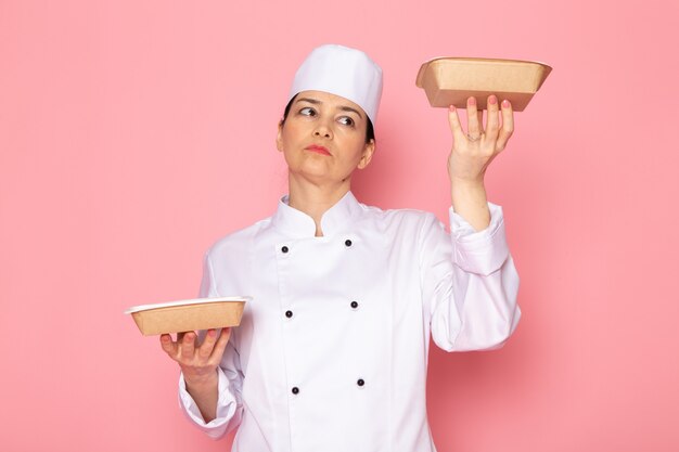 Una vista frontal joven cocinera en traje de cocinero blanco gorra blanca posando sosteniendo cuencos de leche marrón