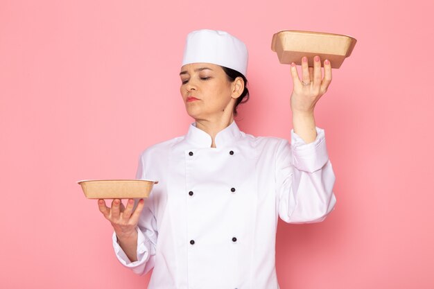 Una vista frontal joven cocinera en traje de cocinero blanco gorra blanca posando sosteniendo cuencos de leche marrón