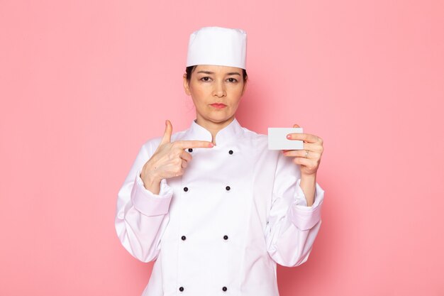 Una vista frontal joven cocinera en traje de cocinero blanco gorra blanca posando con tarjeta blanca