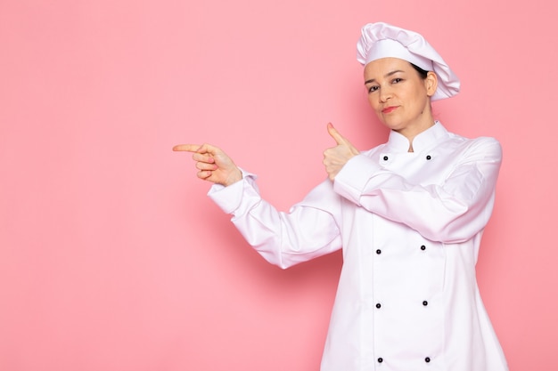 Una vista frontal joven cocinera en traje de cocinero blanco gorra blanca posando