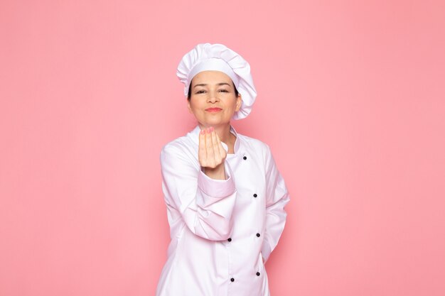 Una vista frontal joven cocinera en traje de cocinero blanco gorra blanca sonriendo posando feliz