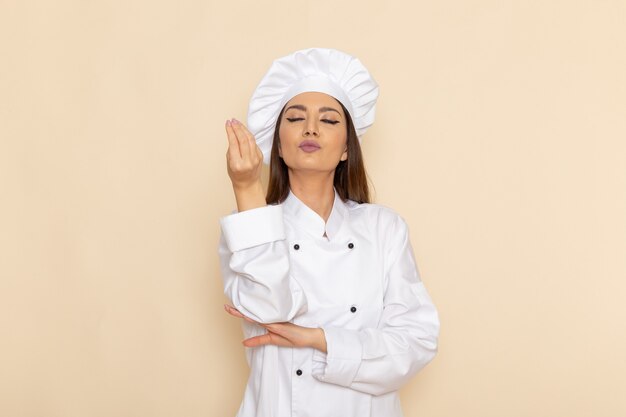 Vista frontal de la joven cocinera en traje de cocinero blanco en la pared blanca