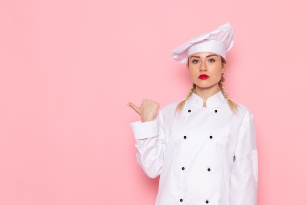 Vista frontal joven cocinera en traje de cocinero blanco simplemente posando en el cocinero espacial rosa