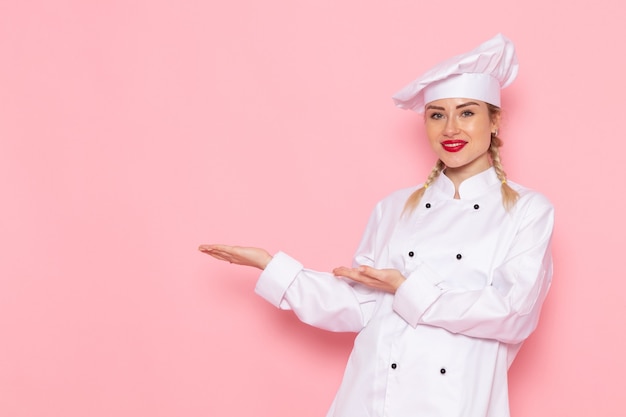 Vista frontal joven cocinera en traje de cocinero blanco sonriendo levemente y posando en el cocinero espacial rosa