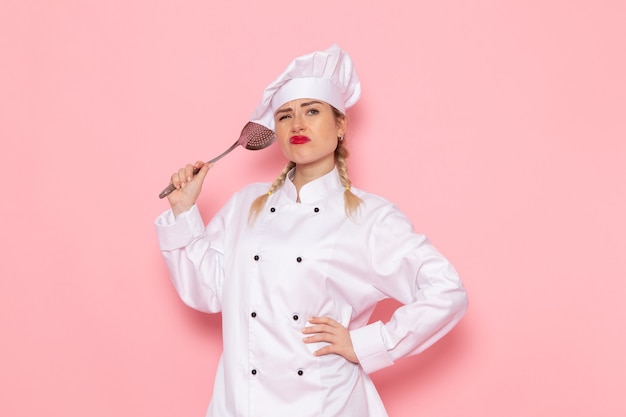 Foto gratuita vista frontal joven cocinera en traje de cocinero blanco sosteniendo una cuchara de plata en el cocinero espacial rosa